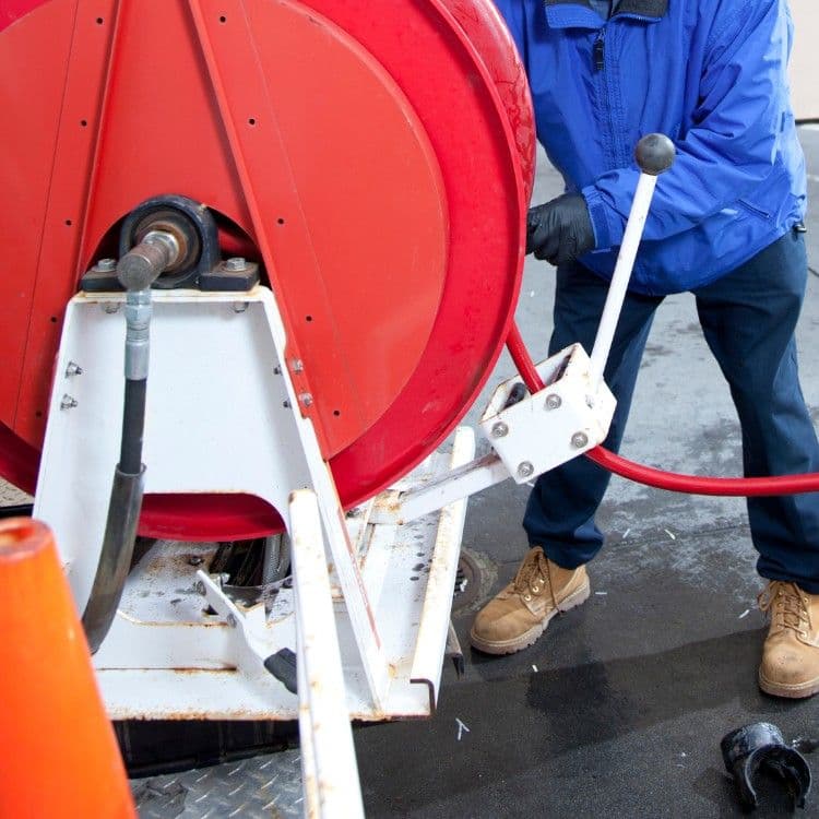 Person operating a red hose reel on a worksite, wearing gloves and blue jacket.