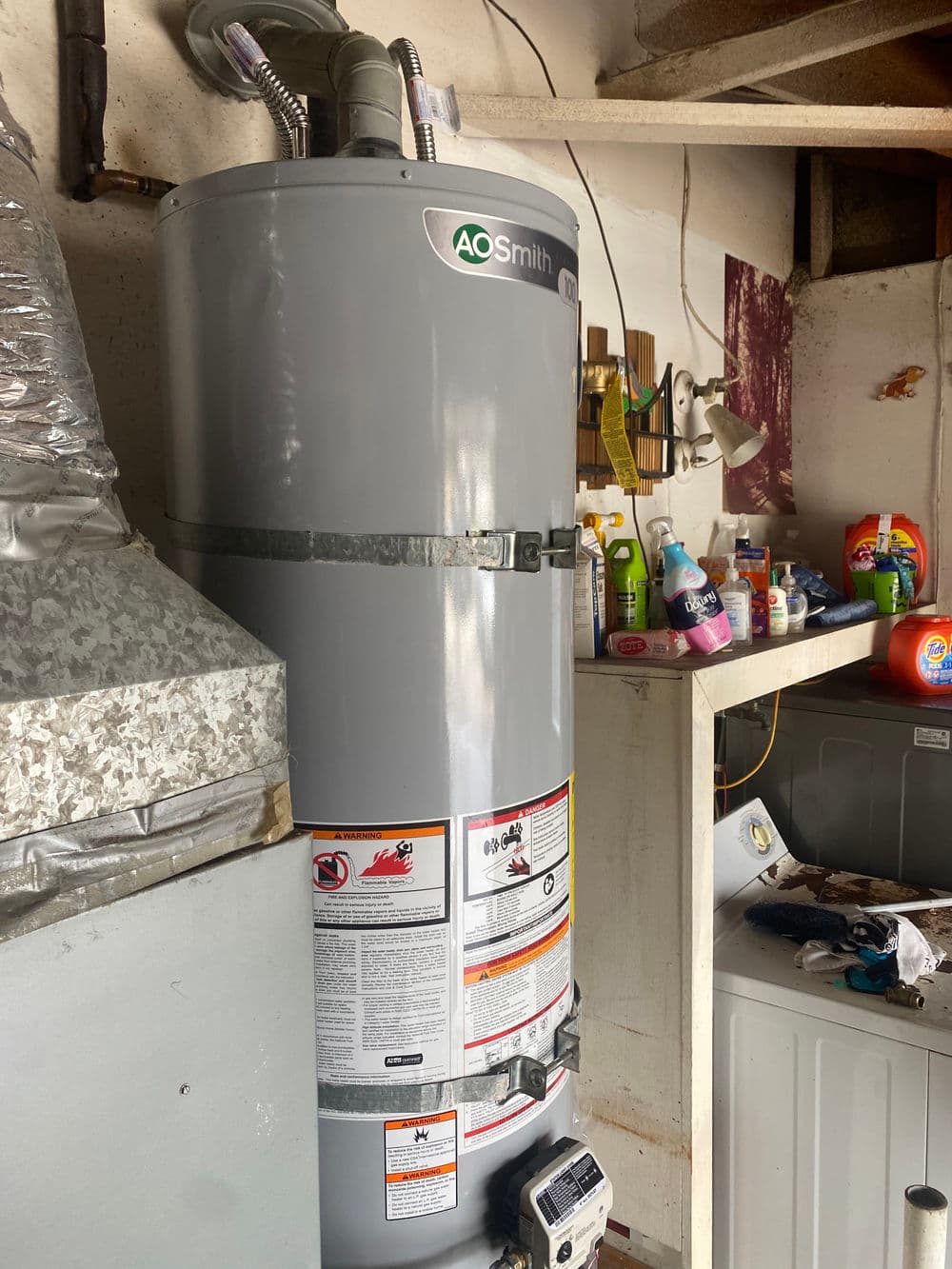 A.O. Smith water heater in a basement, surrounded by cleaning supplies and laundry appliances.