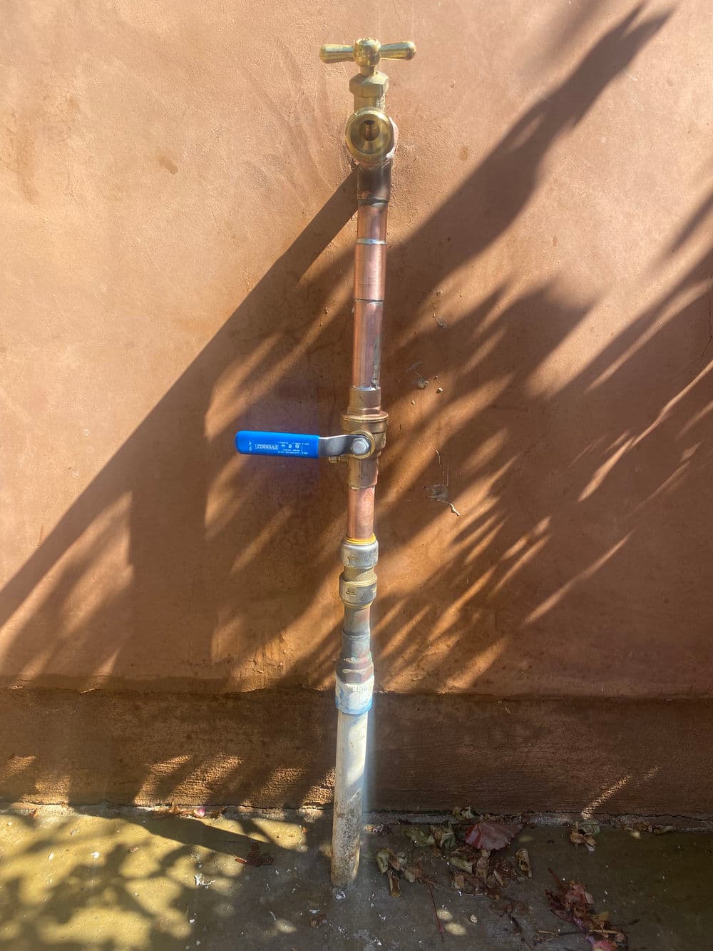 Copper water pipe with valve, positioned against a textured brown wall, casting shadows.