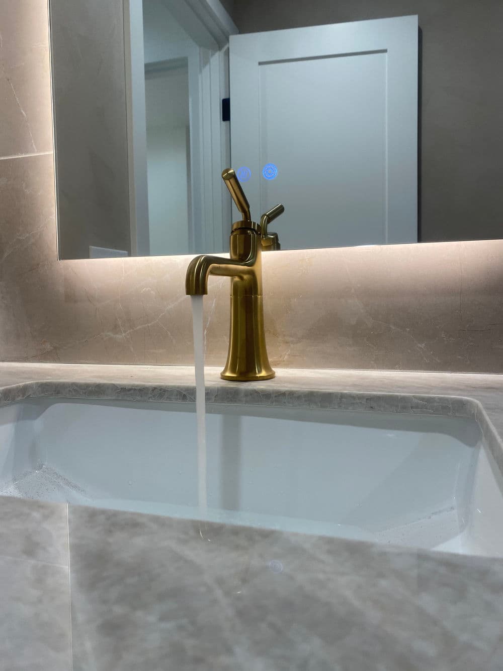 Gold bathroom faucet with running water over a marble sink in a modern setting.
