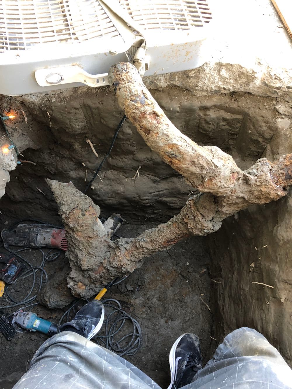 Excavated trench showing a large, rusty pipe in a construction site with tools nearby.