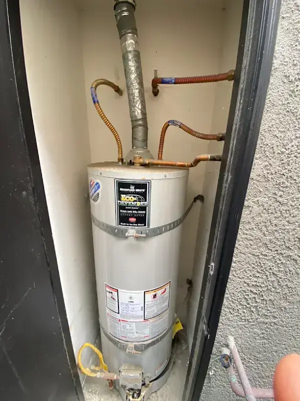 Water heater installation with visible pipes and connections, showcasing a tank-style water heater in a utility space, highlighting Plumbing by Tony's services for residential water heater replacements.