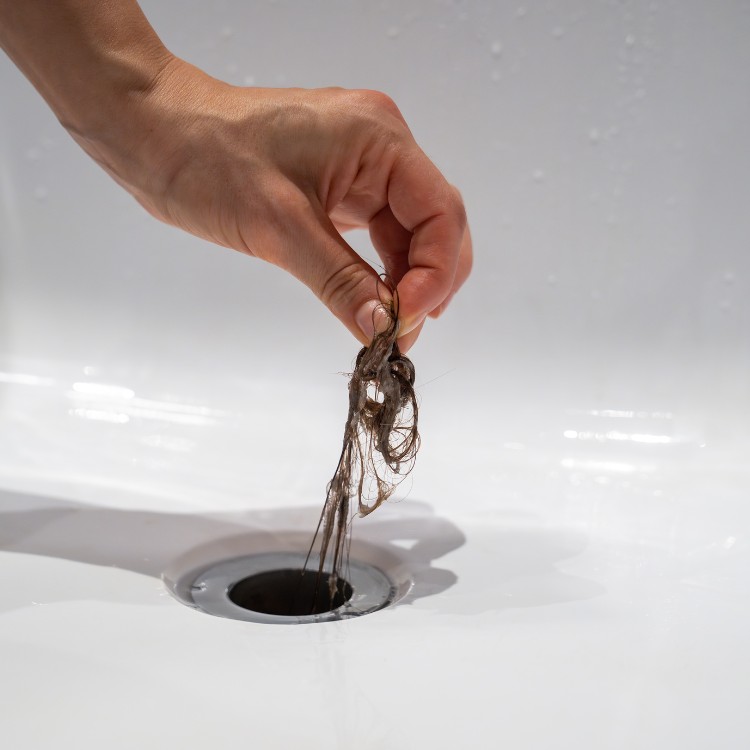 Hand holding hair clump removed from sink drain, illustrating drain cleaning service by Plumbing By Tony.