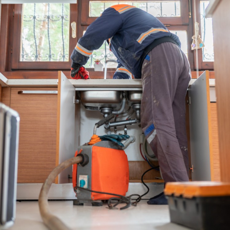 Plumber using hydro jetting equipment under kitchen sink for drain cleaning services.