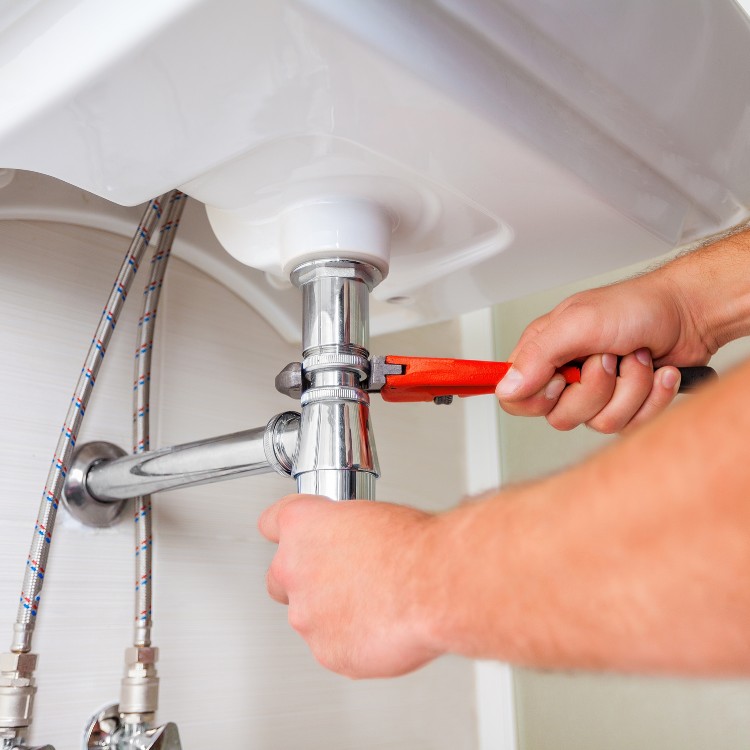 Plumber using a wrench to tighten plumbing under a sink, showcasing professional plumbing services by Plumbing By Tony.