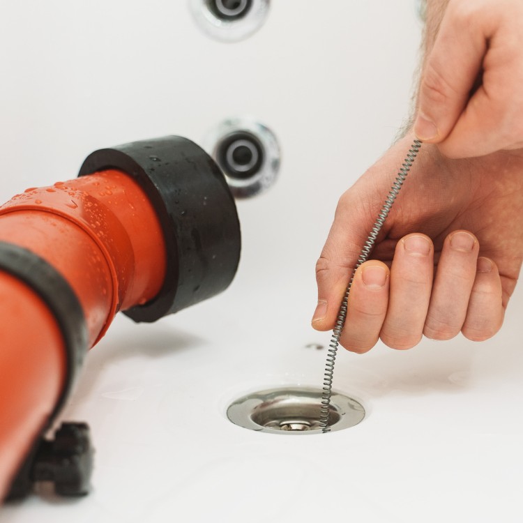 Plumber using a drain snake on a sink, demonstrating drain cleaning services offered by Plumbing By Tony.