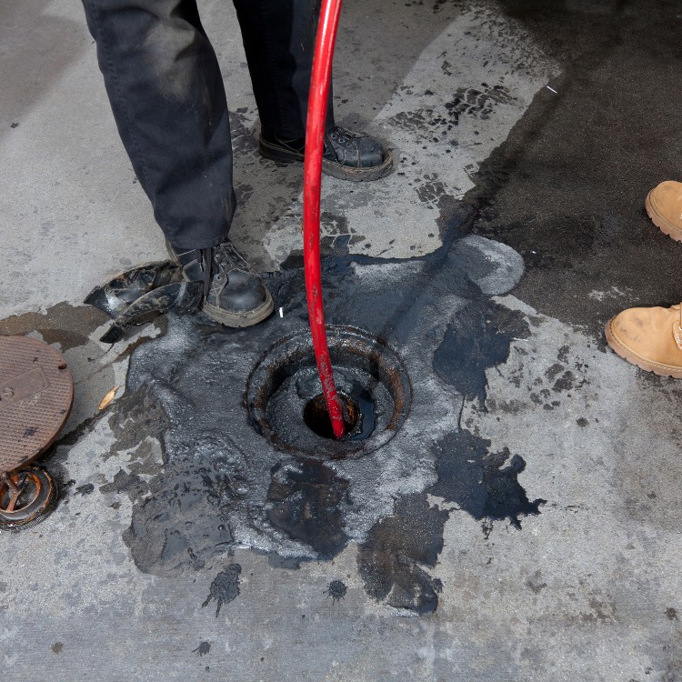 Plumber using a red hydro jetting hose in a drain, demonstrating advanced plumbing techniques for clearing clogs.