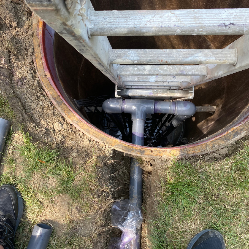 Sewer line access point with ladder, visible pipes and fittings, showcasing trenchless repair methods in Huntington Beach, CA.