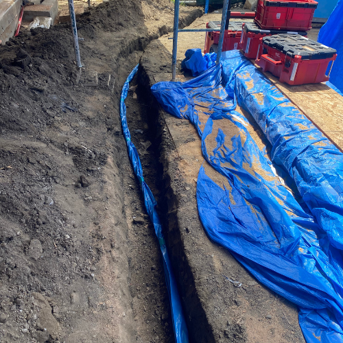 Plumbing By Tony Excavated trench with blue tarps and tools, indicating plumbing preparation for emergency repairs in Huntington Beach.